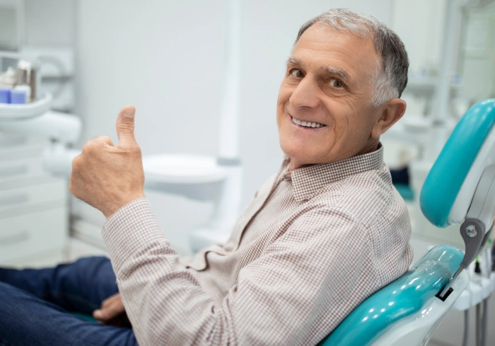 Smiling male patient giving thumbs up in dental chair at orthodontic clinic