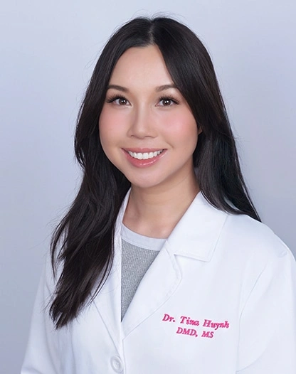 Professional headshot of Dr. Tina Huynh in white dental coat against light background.